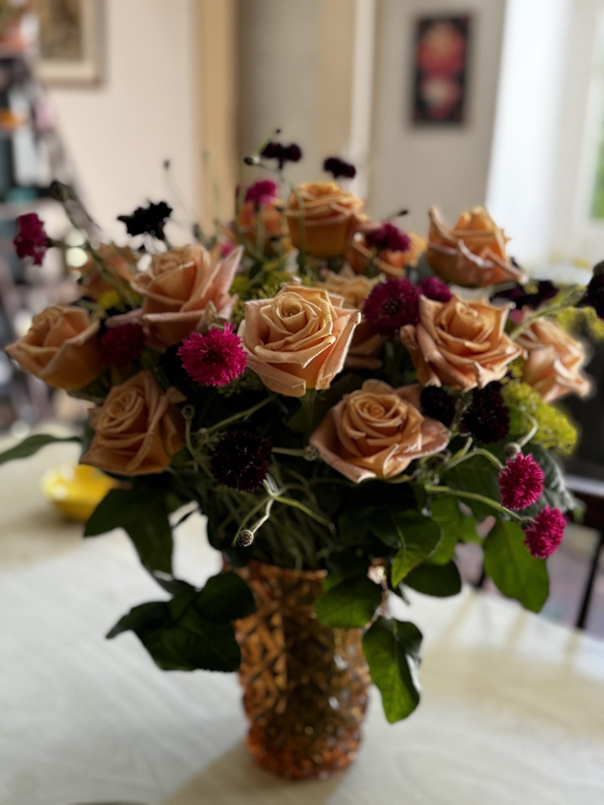 Roses cuivrées et fleurs bordeaux dans un vase, à la maison
